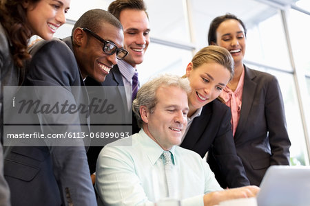 Smiling business people sharing laptop in meeting