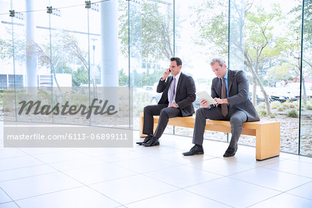 Businessmen using cell phone and digital tablet in lobby Businessmen using cell phone and digital tablet in lobby