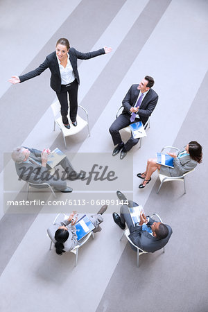 High angle view of businesswoman standing on chair in circle with co-workers