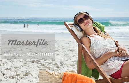 Serene woman listening to headphones in lounge chair on beach Serene woman listening to headphones in lounge chair on beach