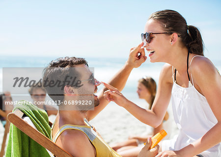 Couple applying sunscreen to each other's nose on beach