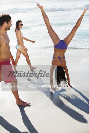 Friends watching woman in bikini doing handstand on beach