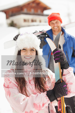 Portrait of smiling couple with skis outside cabin