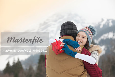 Happy woman holding gift and hugging man with mountains in background
