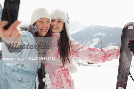 Enthusiastic women with skis taking self-portrait with camera phone in field