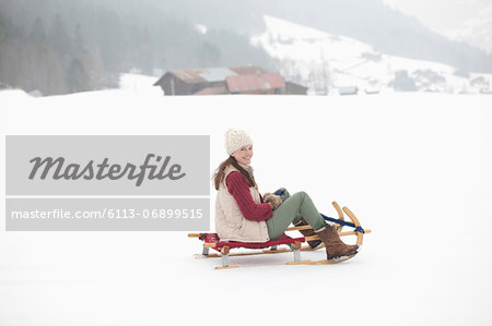 Portrait of smiling woman sledding in snowy field