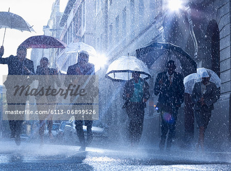 Business people with umbrellas running in rain