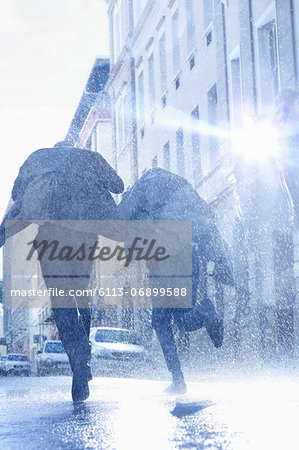 Businessmen with umbrellas running in rainy street