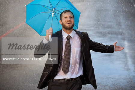 Enthusiastic businessman with tiny umbrella in rainy street