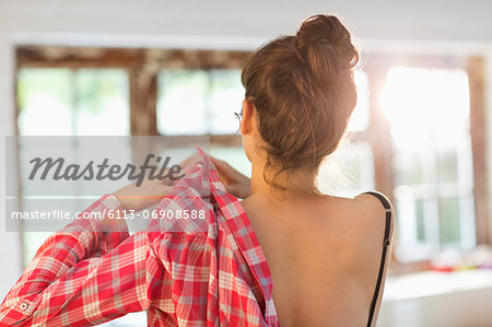 Woman putting on shirt in bedroom