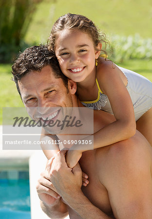 Father and daughter smiling by swimming pool