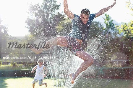 Father and son playing in sprinkler in backyard