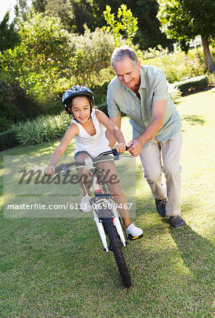 Older man teaching granddaughter to ride bicycle