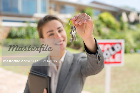 Portrait of realtor holding house keys in front of house