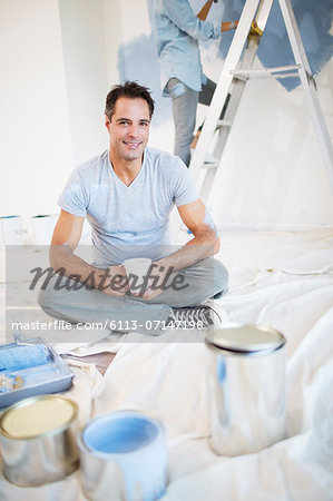 Portrait of smiling man drinking coffee among painting supplies