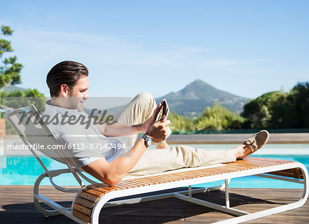 Man using digital tablet on lounge chair at poolside