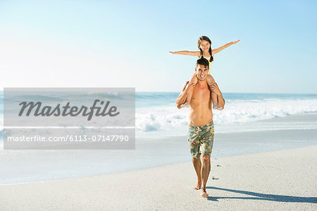 Father carrying daughter on shoulders at beach