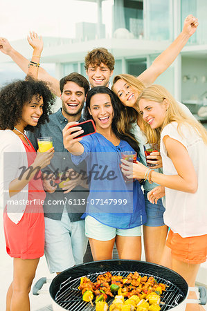 Friends taking self-portrait with camera phone at barbecue