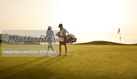 Caddy and woman walking on golf course overlooking ocean