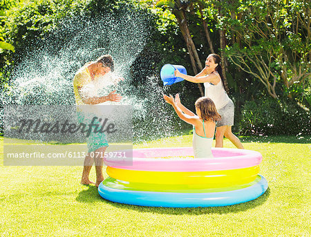 Family tossing water on father in backyard