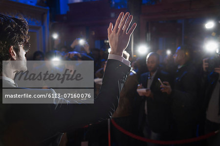 Rear view of male celebrity waving to paparazzi at red carpet event
