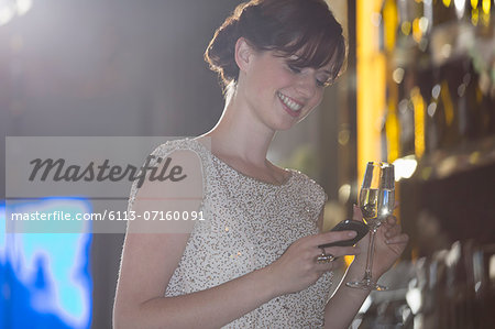 Well dressed woman with champagne looking down at cell phone