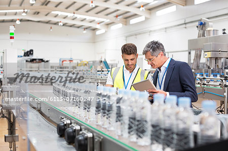 Supervisor and manager watching plastic bottles on conveyor belt