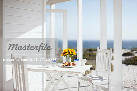 Vase of flowers, coffee and pastries on patio table overlooking ocean Vase of flowers, coffee and pastries on patio table overlooking ocean