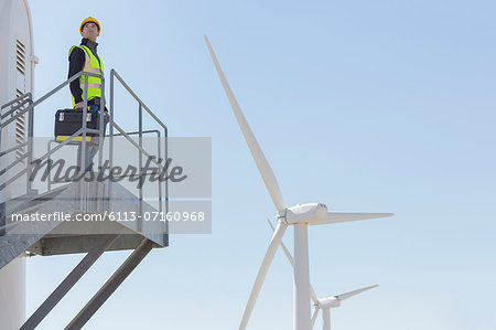 Worker standing on wind turbine in rural landscape