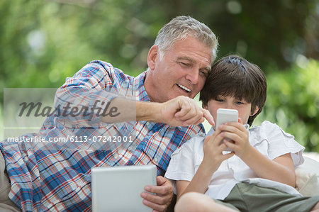 Grandfather and grandson using digital tablet and cell phone