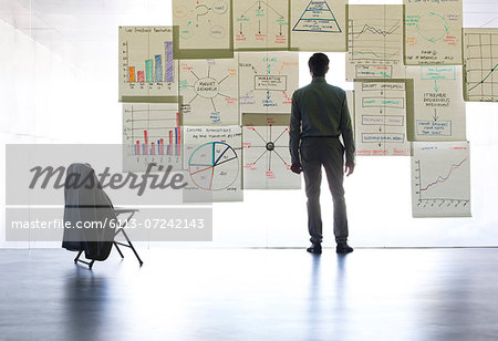 Businessman looking at graphs and charts on glass wall in office Businessman looking at graphs and charts on glass wall in office