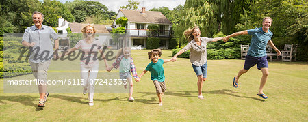 Multi-generation family holding hands and running in grass Multi-generation family holding hands and running in grass