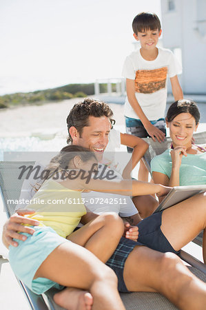 Family using digital tablet on lounge chairs at poolside