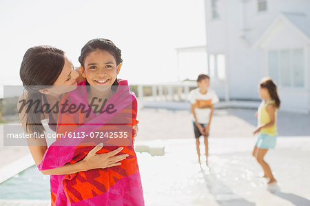 Mother wrapping daughter in towel at poolside