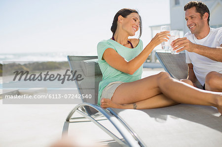 Couple toasting water glasses in lounge chairs at poolside