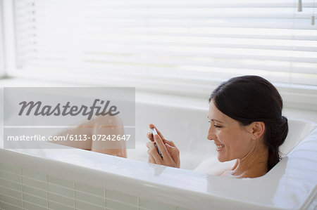 Woman using cell phone in bubble bath