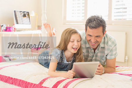 Father and daughter using digital tablet on bed