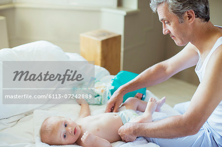 Father changing baby's diaper on bed