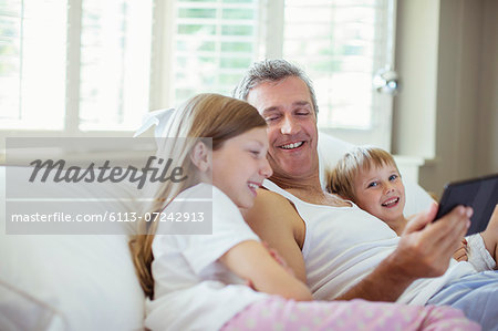 Father and children using digital tablet on bed
