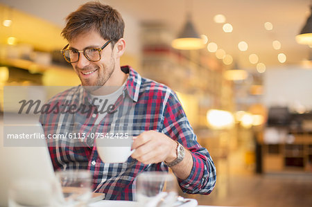 Man using laptop and drinking coffee in cafe