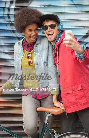 Couple taking self-portrait with cell phone against graffiti wall Couple taking self-portrait with cell phone against graffiti wall