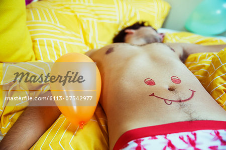 Man with smiley face drawing on belly sleeping after party