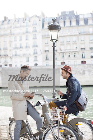 Businessmen with cell phones on bicycles along Seine River, Paris, France