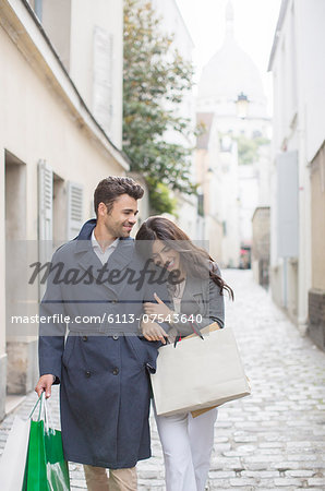 Couple carrying shopping bags on cobblestone street near Sacre Coeur Basilica, Paris, France