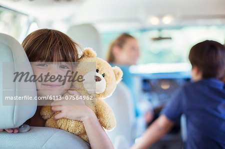 Portrait of happy girl with teddy bear in back seat of car