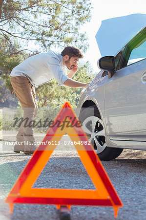 Man at roadside checking car engine behind warning triangle
