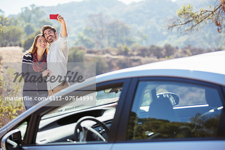 Couple taking self-portrait with cell phone outside car