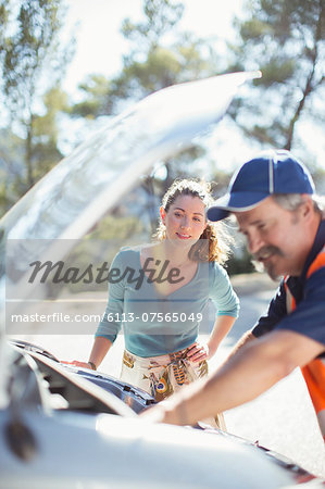 Woman watching roadside mechanic check car engine