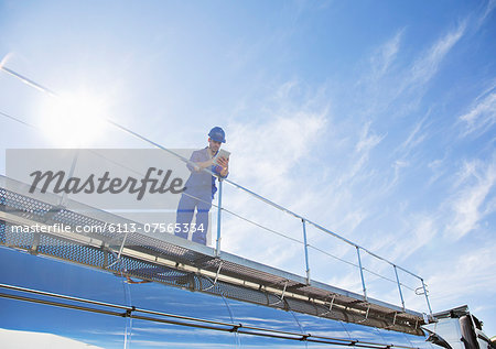 Worker with digital tablet standing on platform above stainless steel milk tanker