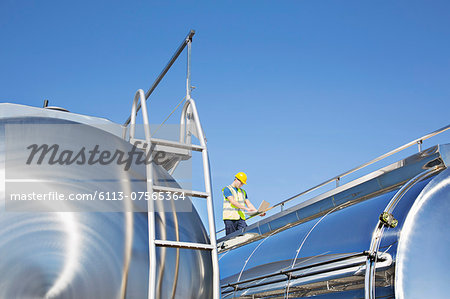 Worker using laptop on platform above stainless steel milk tanker